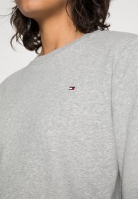 Felpa grigia realizzata in morbido tessuto, con collo rotondo e un piccolo logo ricamato in rosso, bianco e blu sul petto.