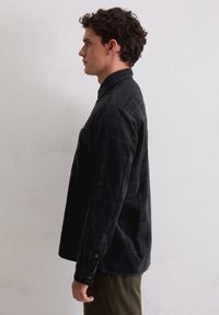 Czarna kraciasta koszula na guziki z kołnierzykiem, długimi rękawami i luźnym krojem. Tkanina wydaje się miękka z teksturowanym wykończeniem.