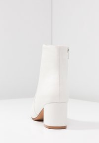 Botín blanco hasta el tobillo con un exterior de cuero liso, puntera redondeada, tacón bajo y ancho, y una cremallera lateral discreta. Diseño moderno y limpio.