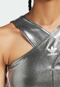 Camiseta atlética de color plateado metálico con un diseño en cruz, que presenta un logo de Adidas en blanco y rayas blancas contrastantes a lo largo de los lados.