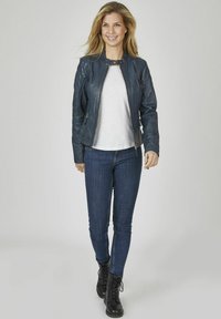 Herrenmarinelederjacke mit körperbetontem Schnitt und Reißverschluss vorne, kombiniert mit einem weißen Hemd und dunkelblauen Skinny-Jeans sowie schwarzen Schnürstiefeln.