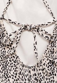 Lahka tkanina s črno-belo leopardjo vzorcem, z nabranim dekoltejem, zavezanjem na hrbtu in gladko teksturo.