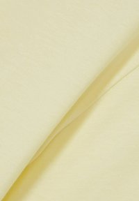 Stof de un galben deschis, cu o textură netedă, pliat pentru a arăta adâncimea. Materialul pare moale și ușor elastic, cu o finisare uniformă.
