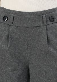 Pantalon gris taille haute avec plis sur le devant, ceinture avec passants et boutons noirs de chaque côté.