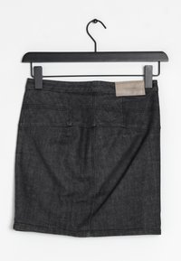 Jupe en denim foncé sur un cintre noir. Présente un design structuré, une légère forme évasée, des poches arrière et une étiquette en cuir près de la taille.