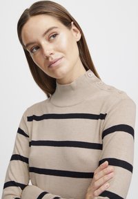 Maglione beige a collo alto con righe orizzontali navy, dotato di dettagli con bottoni sul colletto. Tessuto in maglia morbida con silhouette aderente.