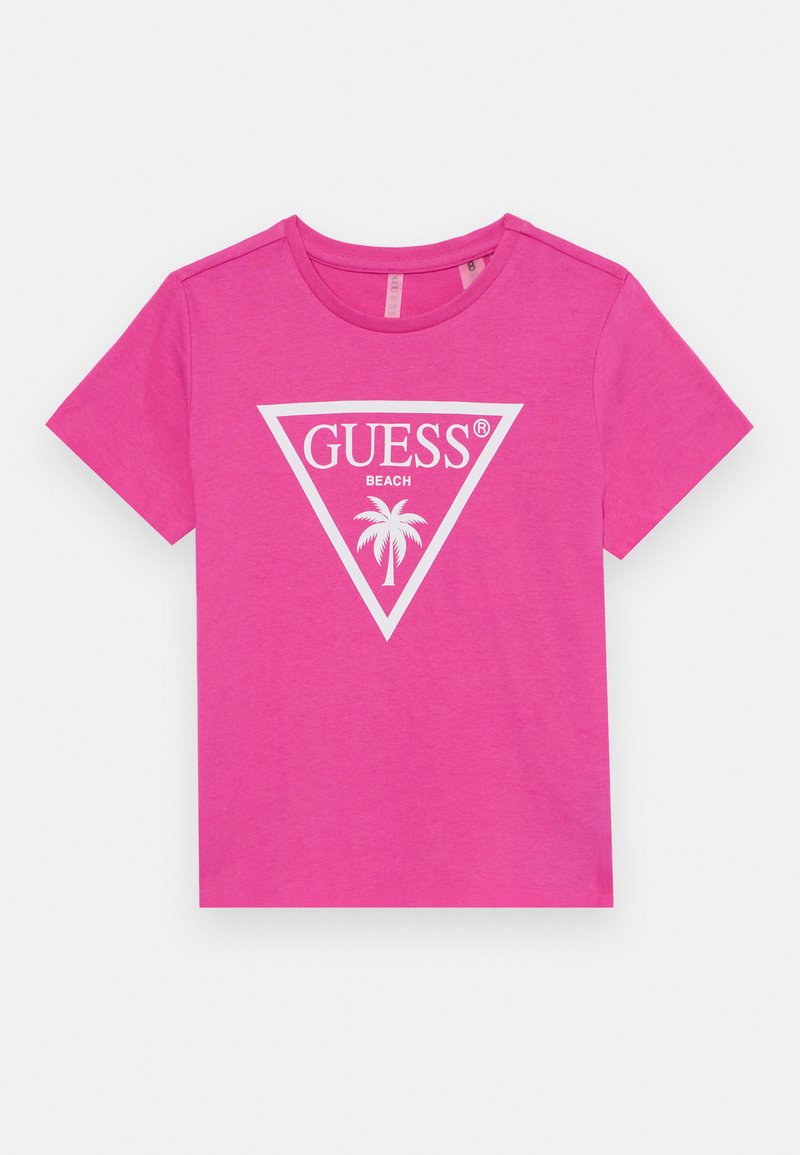 Rožinė medvilninė marškinė su balta trikampio forma logotipu, ant kurio užrašyta "GUESS BEACH", ir palmės grafika centre. Trumpomis rankovėmis ir apvaliu iškirpimu.