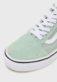 Zapatillas de ante verde claro con cordones blancos, suela de goma negra y acentos en blanco a contraste en el lateral y en la puntera.