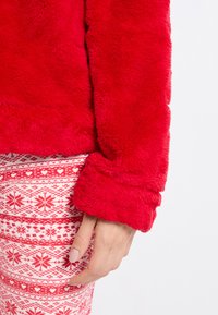 Červený plyšový svetr s měkkou texturou a manžetovými rukávy, zkombinovaný s vzorovanými bílými a červenými kalhotami se srdíčky a sněhovými vločkami.