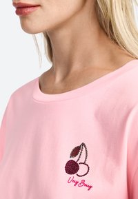 Lyserød bomulds t-shirt med bred halsudskæring, der prydes af et kirsebærmotiv og teksten "Very Berry" i rød broderi. Glat tekstur og afslappet design.