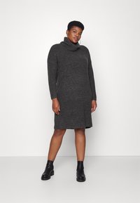 Vestido cinza de malha com gola alta e mangas compridas. Apresenta um corte reto e uma bainha ligeiramente assimétrica. Combinado com botas pretas até ao tornozelo.