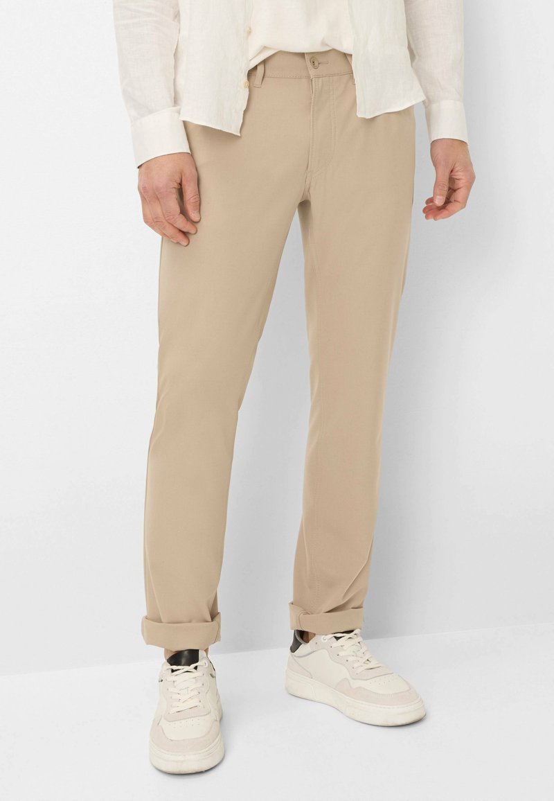 Beige chino's met een rechtvallend ontwerp, gemaakt van zachte stof. Voorzien van een knoopsluiting en opgerolde pijpen, gecombineerd met witte sneakers.