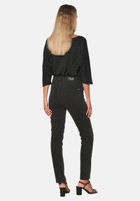 Svarta högmidjade jeans med slim fit och subtil textur, kombinerat med en lös svart glittrig topp, sedd bakifrån.