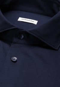 Polo bleu marine à boutons avec un col et une étiquette blanche indiquant "seidensticker" à l'intérieur de l'encolure.