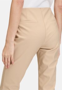 Béžové tailored kalhoty vyrobené z hladkého materiálu, s vysokým pasem a zadními kapsami, s čistými liniemi a přiléhavým střihem.