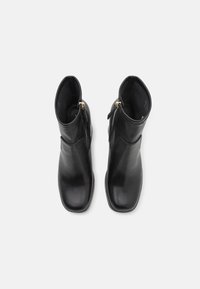 Botas de tobillo de cuero negro con una textura suave, que presentan un cierre lateral y una suela plana. El diseño es elegante con una puntera cuadrada.