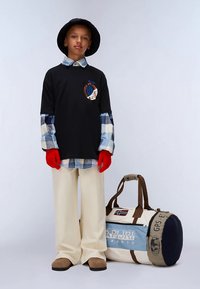 Sort langærmet skjorte med grafik, blåternet skjorte under, cremefarvede brede bukser, røde handsker, brune loafers og en duffel taske.