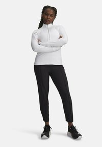Witte sportieve lange mouw top met een half-rits kraag, gecombineerd met aansluitende zwarte broek en zwarte sneakers met witte accenten. Gladde textuur.