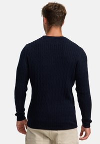 Marineblå kabelstrikket genser med en ribbet tekstur, lange ermer og rund hals. Perfekt for lag-på-lag bruk i kaldere forhold.