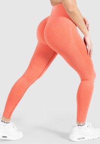 Hoge taille, getextureerde legging in een felle koraalkleur, met een getailleerd ontwerp en naden, gecombineerd met witte sportschoenen.