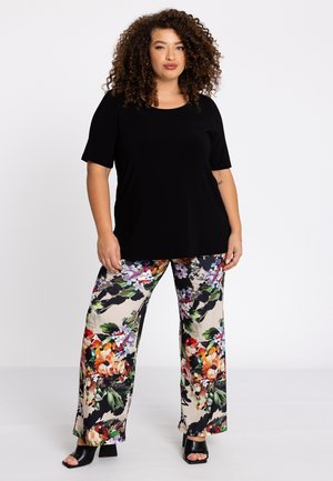 Un haut noir à manches courtes associé à un pantalon floral à jambes larges mettant en avant des fleurs multicolores vibrantes sur un fond clair. Des talons ouverts noirs.
