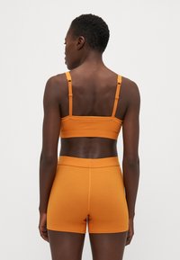 Bralette arancione a coste con spalline regolabili abbinato a pantaloni corti a coste. Texture liscia, tessuto elastico e design aderente.