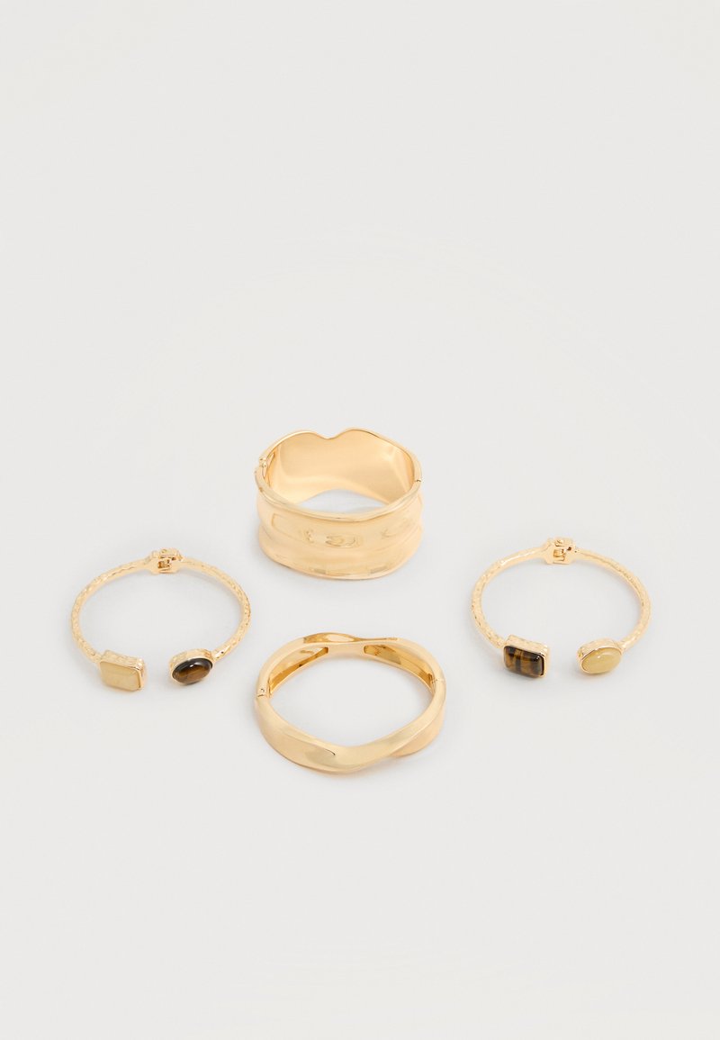 Quatre bracelets en or sur un fond blanc, deux avec des motifs ondulés et deux avec des pierres sombres ovales et rectangulaires.