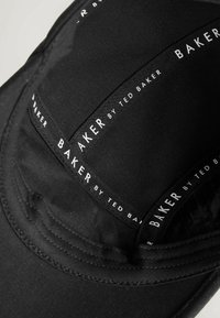 Must kangastämblemüts valge trükitud tekstiga "BAKER BY TED BAKER" sisemise õmbluse ja ääre ümber.