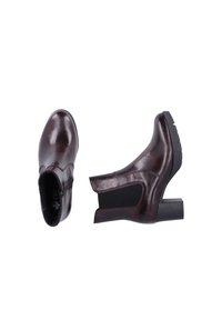 Bottines en cuir bordeaux avec un talon block, fermeture éclair sur le côté et panneaux élastiques pour plus de flexibilité. Texture lisse avec une finition brillante.