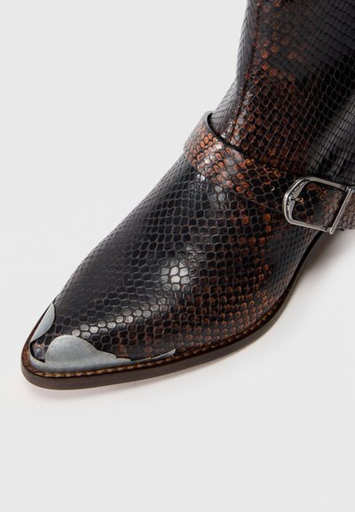 Melna un brūna čūsku raksta ādas zābaks ar norādītu purngalu, sudraba aparatūru un sprādzes siksnu ap potīti. Tekstūrēts apdare.