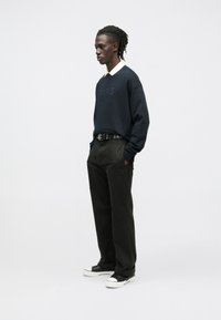 Sudadera azul marino oscuro con el logo "PARIS" en relieve, combinada con pantalones anchos negros, cinturón con herrajes plateados y zapatillas negras con suela blanca.