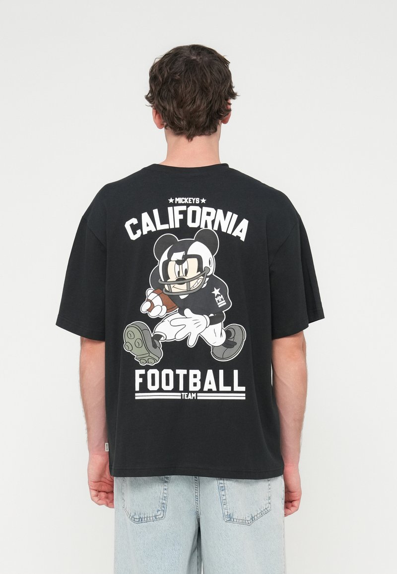 Μαύρο βαμβακερό μπλουζάκι με γραφικό που απεικονίζει έναν χαρακτήρα κινουμένων σχεδίων να παίζει ποδόσφαιρο, με το κείμενο "CALIFORNIA FOOTBALL TEAM" σε λευκό χρώμα.