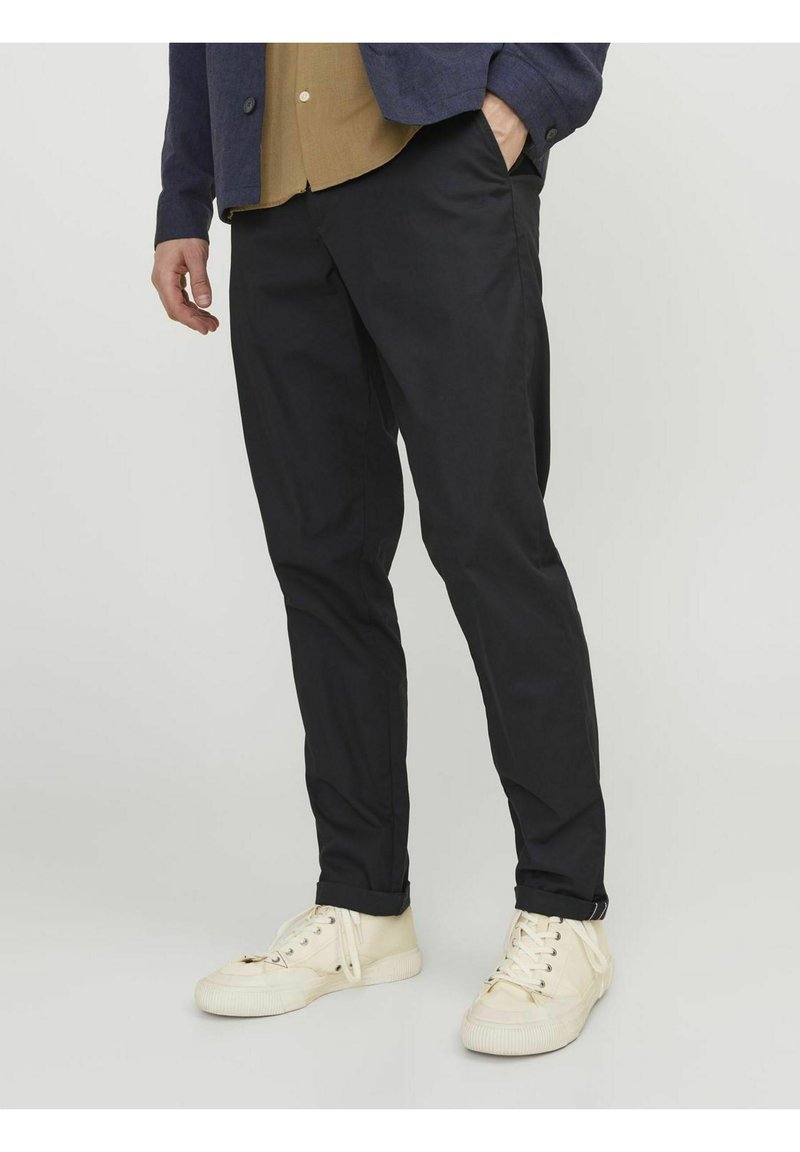 Pantaloni neri realizzati in tessuto leggero, caratterizzati da una vestibilità slim e tasche laterali. Indossati con sneakers color crema e una camicia con colletto.