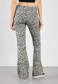 Flared jeans laget av myk stoff, med et grått og hvitt leopardmønster, baklommer og en standard linning.