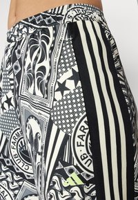 Οι μαύρες και λευκές μοτίβες φόρμες διαθέτουν έναν συνδυασμό γεωμετρικών σχεδίων, κυμάτων και λογότυπων, με αντίθετες μαύρες ρίγες στο πλάι και ελαστική ζώνη στη μέση.