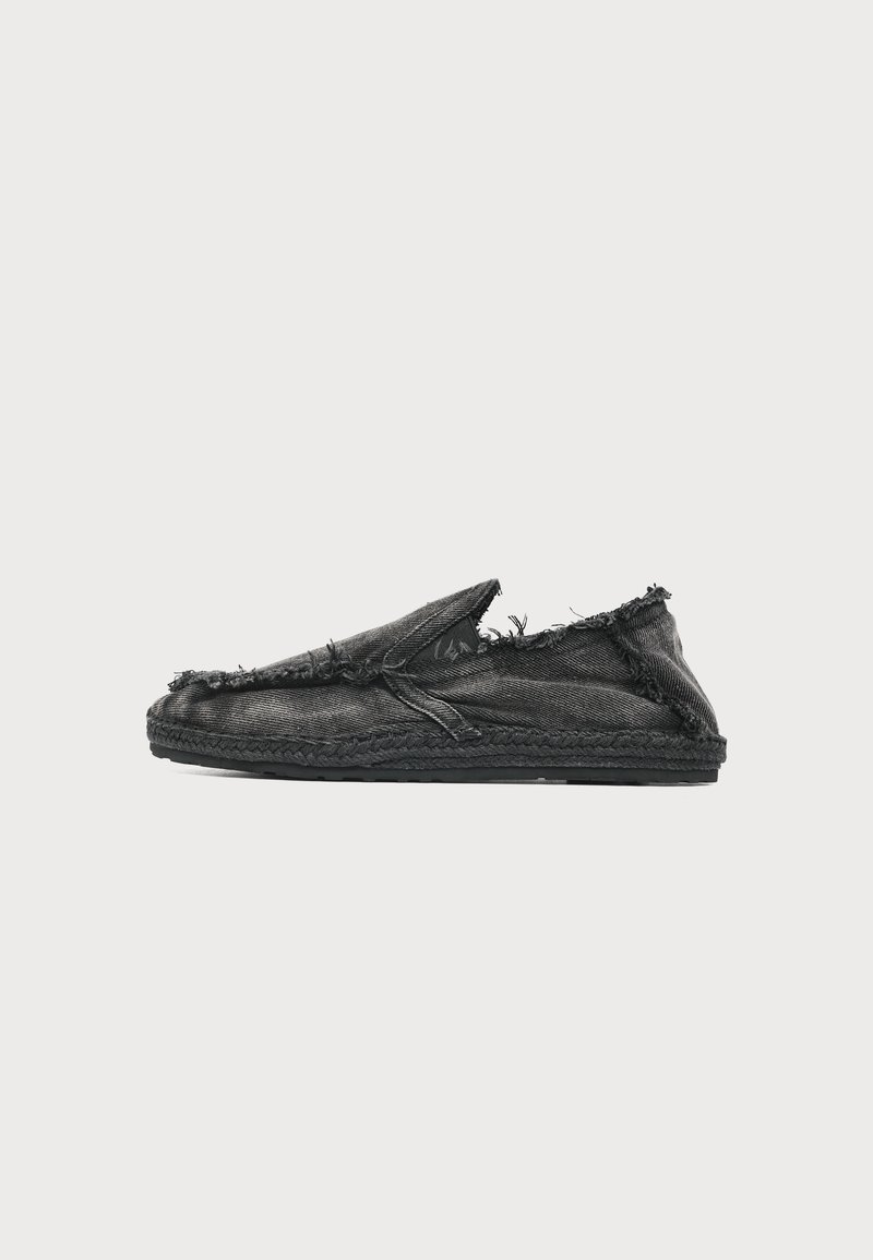 Chaussure slip-on en denim noir avec bords effilochés et semelle tissée, vue de côté sur fond blanc.