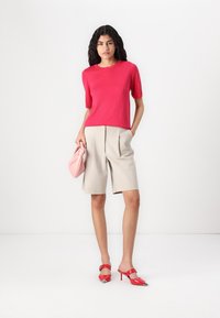 Red short-sleeved top, beige pleated shorts, red high-heeled shoes with pointed toes, and a light pink clutch. Plain white background.