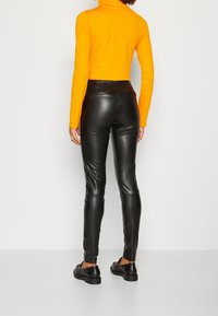 Black faux leather leggings with a slim fit, featuring a high waist and back pockets, paired with a bright orange turtleneck top.