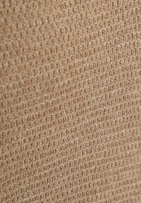 Gestructureerde stof in een lichte beige kleur, met een geweven patroon van kleine lussen dat een zachte, tactiele oppervlakte creëert.