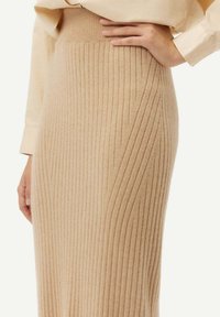 Beige ribbad stickad kjol med hög midja, som har vertikala ränder och en mjuk textur. Designad för en figurnära silhuett.