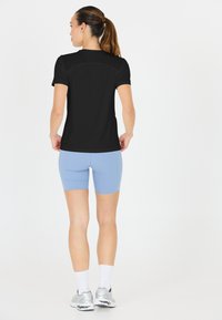 Sort kortærmet træningsskjorte med en sømløs design, parret med lyseblå cykelshorts. Har hvide sokker og sølvfarvede sneakers.