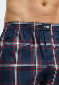 Boxer in fantasia a quadri blu navy con strisce rosse, verdi e bianche; vita elastica con etichetta nera recante la scritta "BOSS."
