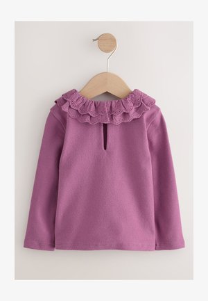 Bluza mov cu mâneci lungi și un guler cu volane, având o deschidere tip cheiță în spate. Confecționată dintr-un material moale cu o textură netedă.