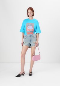 Φωτεινό μπλε υπερμεγέθη t-shirt με γραφικό τύπωμα, σκισμένα τζιν σορτς, μαύρα μυτερά φλατ παπούτσια και μια μικρή ροζ τσάντα.