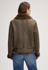 Bruine shearling jas met een bontkraag, voorzien van leren accenten en een gestructureerde afwerking. Gestyled met jeans met rechte pijpen.