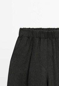 Pantalon en lin noir avec taille élastique, doté de poches latérales et d'une surface texturée. Le design est simple et minimaliste.