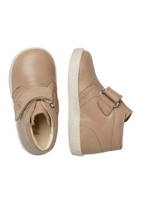 Scarpe in pelle tan con una texture morbida. Il design include una fascia con hardware metallico e una suola leggermente elevata in gomma bianca testurizzata.