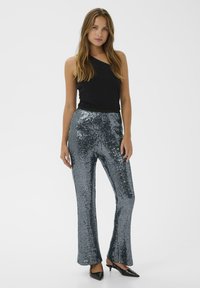 Black ribbed one-shoulder top paired with shiny, silver sequin flared trousers. The outfit is completed with black pointy-toed shoes.