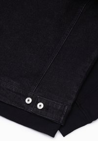 Manche de veste en jean noire avec deux boutons-pression argentés et poignet côtelé noir sur fond blanc.