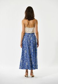 Mėlyna gėlių maksimalistė sijonas su susiraukšlėta liemene ir piešiniu. Pora su kreminės satino camisolė, kuri turi plonas juosteles.